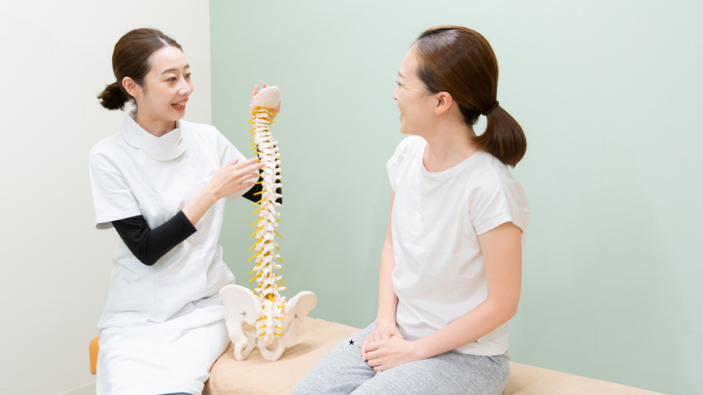 整体師が脊椎模型（背骨の模型）を使って、患者に骨格の歪みについて笑顔で説明しているカウンセリング風景。